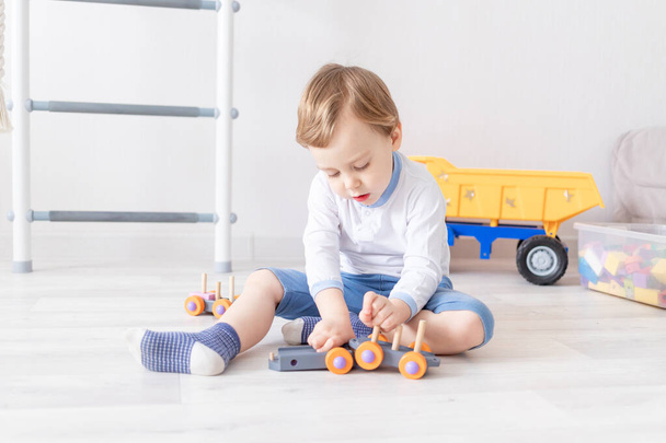 chlapeček hrající si s dřevěnými hračkami doma na podlaze - Fotografie, Obrázek