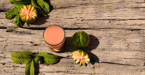 Closeup of Vitamin C rich Fresh Pink Guava juice with guava fruits in a isolated wooden background with copy space for inscription. Summer refreshment. Fresh juice. - Photo, Image