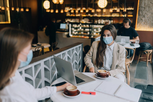 Two pretty women wearing medical face mask, using laptop to work. - Photo, Image