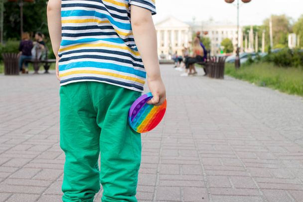 Un petit enfant tient un jouet anti-stress pop il avec une place pour le texte dans le fond du parc de la ville. - Photo, image