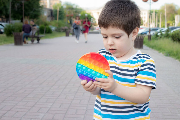 Un bambino di 4 anni gioca con Pop It nel parco cittadino. Giocattolo antistress per lo sviluppo di capacità motorie fini nei bambini. - Foto, immagini