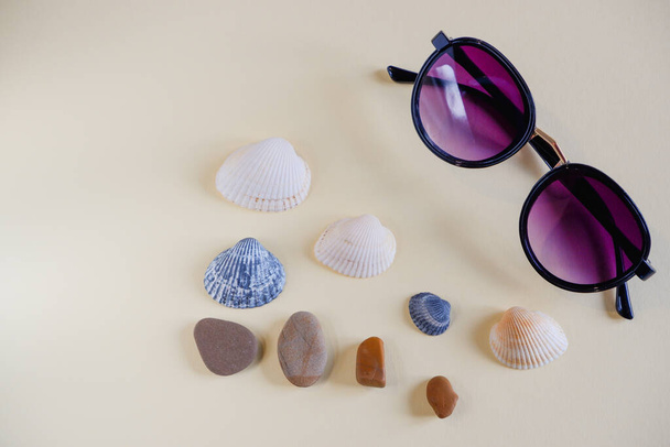 海の休暇の概念。平置きだ。パステルイエローの背景にサングラス、石や貝殻。テキストの場所. - 写真・画像