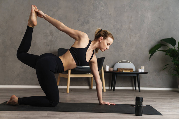 Jovem mulher saudável atraente praticando ioga em um tapete no estúdio, em uma posição de ioga - Foto, Imagem