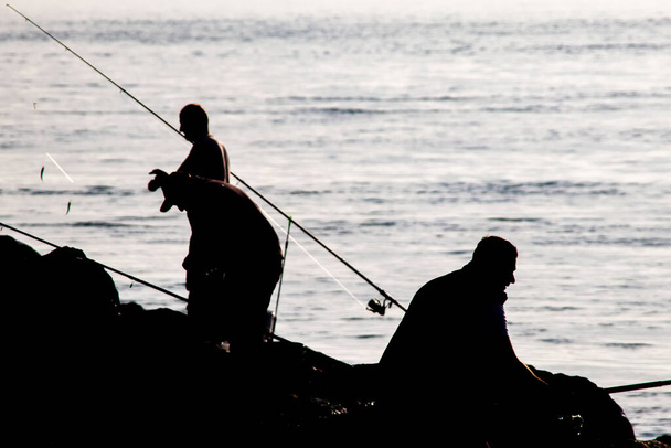 Silhouette di pescatori dilettanti con canne da pesca in riva al mare nelle prime ore del mattino. - Vettoriali, immagini