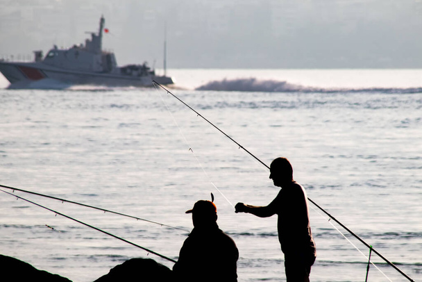 Силуэты рыбаков-любителей с удочками на берегу моря ранним утром. - Вектор,изображение