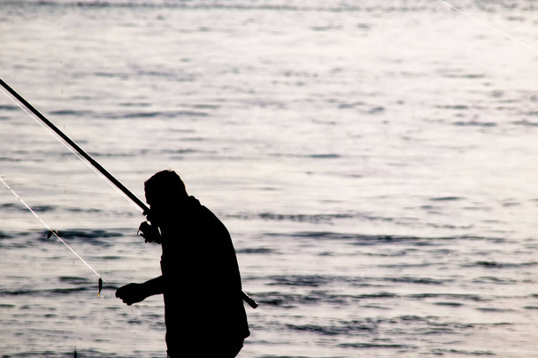 Amatőr halászok sziluettjei horgászbotokkal a tengerparton kora reggel. - Vektor, kép