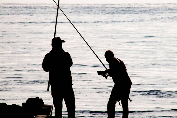 Silhouettes of amateur fishermen with fishing rods on the seashore in early morning time. - Vector, Image
