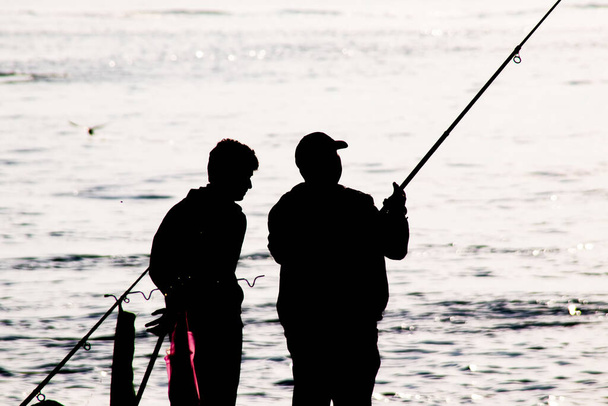 Σιλουέτες ερασιτεχνών ψαράδων με καλάμια ψαρέματος στην παραλία νωρίς το πρωί. - Διάνυσμα, εικόνα