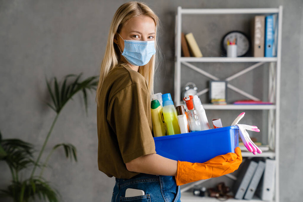 Blonde european woman in face mask posing with cleaning product at home - Foto, immagini