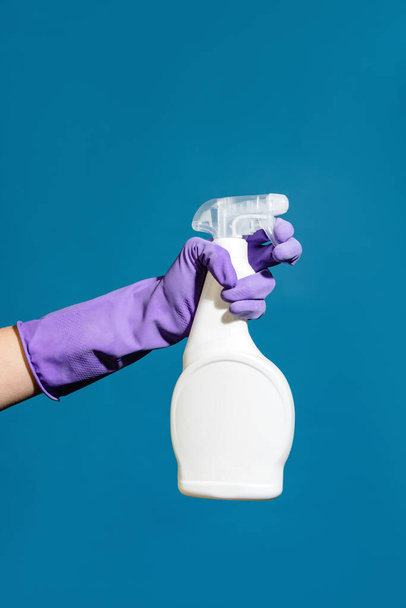 Closeup photo of hand wearing glove and cleaning spray isolated over blue wall - Foto, afbeelding