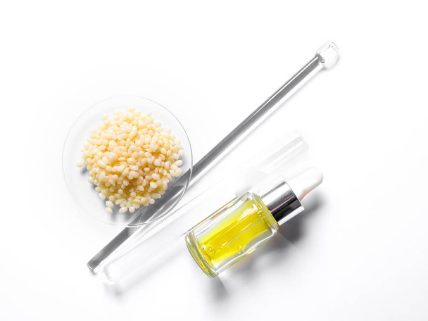 Candelilla Wax in Chemisch Horlogeglas, gele cosmetische vloeistof (olie) en reageerbuis plaats naast roerstaaf. Chemicaliën voor schoonheidsverzorging op witte laboratoriumtafel. (bovenaanzicht) - Foto, afbeelding