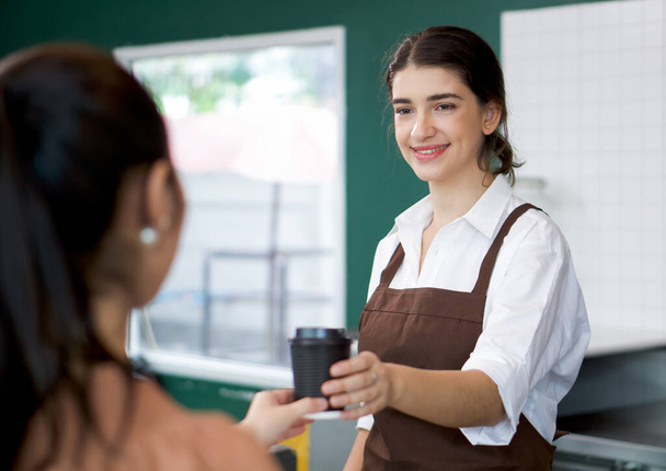 Caucasiano barista vestido com avental serve café quente para jovens clientes asiáticos. Atmosfera da manhã em um café. - Foto, Imagem