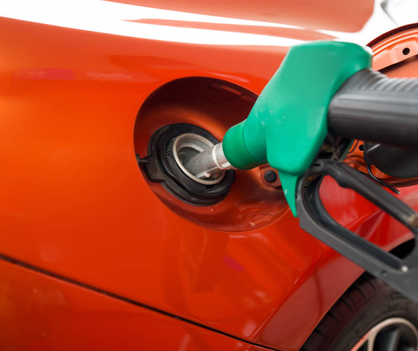 Green benzene gas pump nozzle filling up orange sport car tank. Close up - Photo, Image