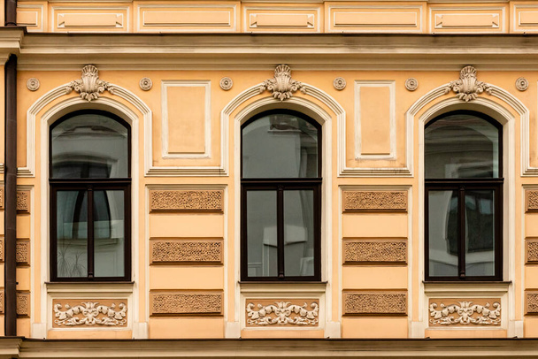 Detail der gelb-cremefarbenen Jugendstilfassade von drei Fenstern, die die Fassade gegenüber der Straße in Riga, Lettland, Europa widerspiegeln - Foto, Bild