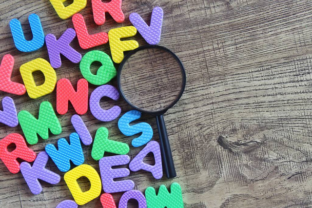 Bovenaanzicht van vergrootglas en kleurrijk alfabet op houten tafel. Kopieer ruimte voor tekst. - Foto, afbeelding