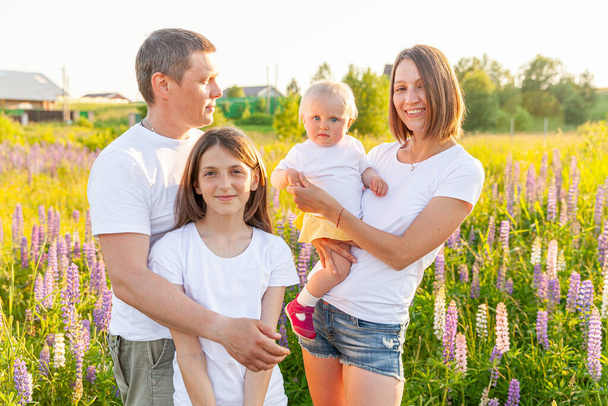 Happy family mother father embracing kids outdoor. Woman man baby child and teenage girl on summer field with blooming flowers background. Happy family mom dad and daughters playing on meadow - Photo, Image