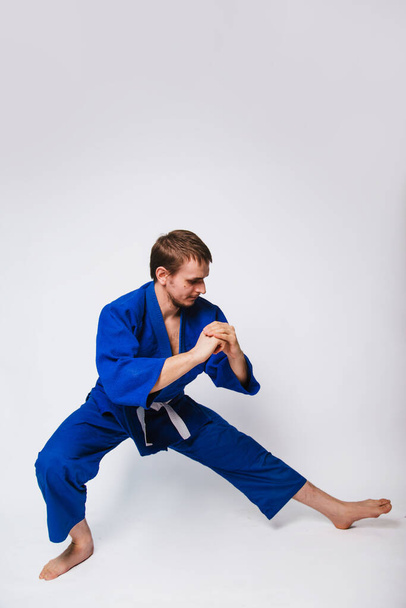 Junger Mann im blauen Kimono auf weißem Hintergrund. Der Typ ist neu im Kampfsport. Studioaufnahme - Foto, Bild