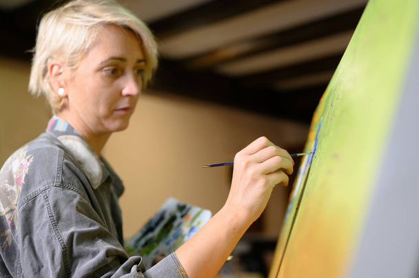 Kobieta artysta artysta malarz skoncentrowany i natchniony obraz malarski z pędzlem i kolorami olejnymi na płótnie. - Zdjęcie, obraz