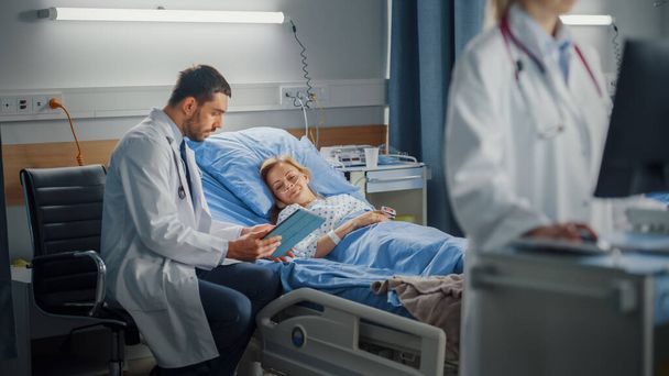 Hospital Ward: Professional Female Doctor Uses Medical Computer. In the Background Modern Equipment Clinic Surgeon Using Tablet Computer Consulting Patient Recovering After Successful Surgery in Bed - Фото, зображення
