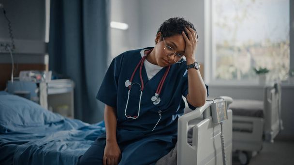Hospital Ward: Portrait of Sad, Tired Black Nurse Sitting on a Bed, Holding Her Head in Sorrow for all the Patients that Couldnt Be Saved in Pandemic. During Tragic Times Brave Paramedics Save Lives - Zdjęcie, obraz