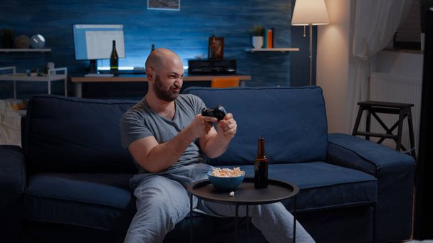 Päättäväinen innoissaan mies istuu sohvalla pelaa videopelejä - Valokuva, kuva