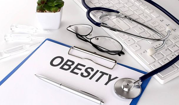 OBESITY text on white paper on the white background. stethoscope ,glasses and keyboard - Photo, Image
