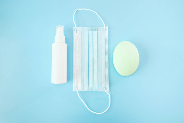 Novel corona virus fighting prevention concept. Top above overhead close up view photo of face mask bottle with spray and bar of white soap isolated over blue background - 写真・画像