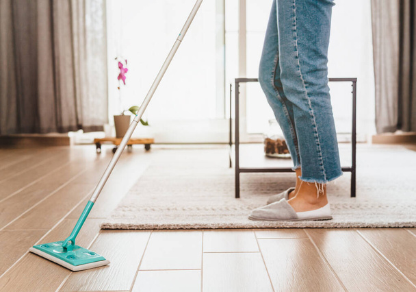 Vrouw in casual kleding reinigt de woonkamer met een stofbezem - Foto, afbeelding