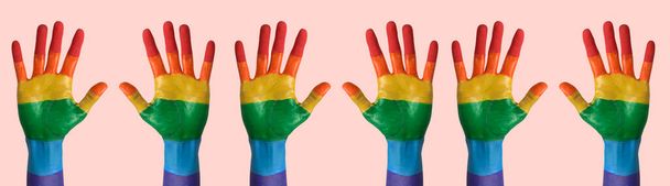 sommige paar opgeheven handen geschilderd als de regenboogvlag tegen een lichtroze achtergrond, in een panoramisch formaat te gebruiken als webbanner of header - Foto, afbeelding