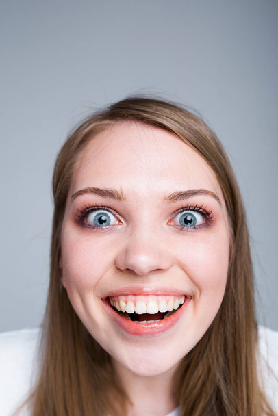 Фото крупным планом. Девушка с белоснежной улыбкой широко раскрывает рот и удивляется, глядя в камеру. - Фото, изображение