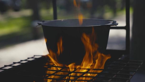 Кухонний горщик стоїть на решітці з великим полум'ям вогню, готує на відкритому повітрі в каструлі, зовнішні туристичні рецепти, вогняна страва на вихідних, відпочиває в лісі
 - Фото, зображення