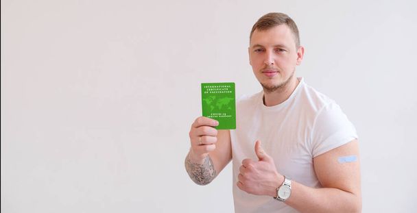 緑色の国際予防接種証明書を背景にTシャツを着た成人男性。Covid-19に対する予防接種の証拠として免疫パスポートを旅行する. - 写真・画像