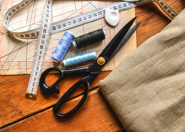 herramientas de coser, tijeras, carretes de hilo, cinta métrica se encuentran en los diagramas de sastres y una mesa de madera - Foto, imagen