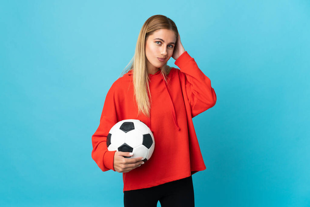 Νεαρή γυναίκα ποδοσφαιριστής απομονωμένη σε μπλε φόντο έχοντας αμφιβολίες - Φωτογραφία, εικόνα