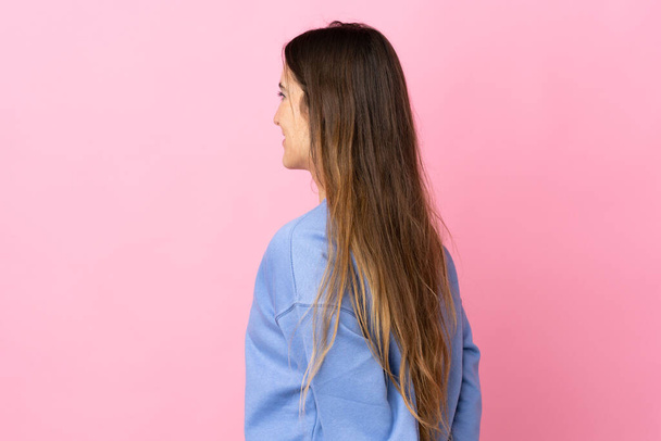 Young caucasian woman isolated on pink background in back position and looking back - 写真・画像