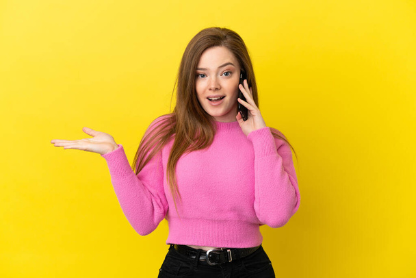 Teenager girl using mobile phone over isolated yellow background having doubts while raising hands - Foto, Imagem