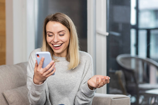 Portrait excited young woman winner screaming yes rejoicing success looking at cellphone. Happy overjoyed woman holding mobile phone celebrate good news surprise bid win app victory sit on sofa at hom - Fotografie, Obrázek