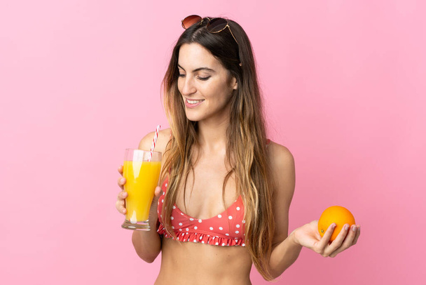 Young blonde woman over isolated pink background in swimsuit and holding a cocktail - Photo, Image