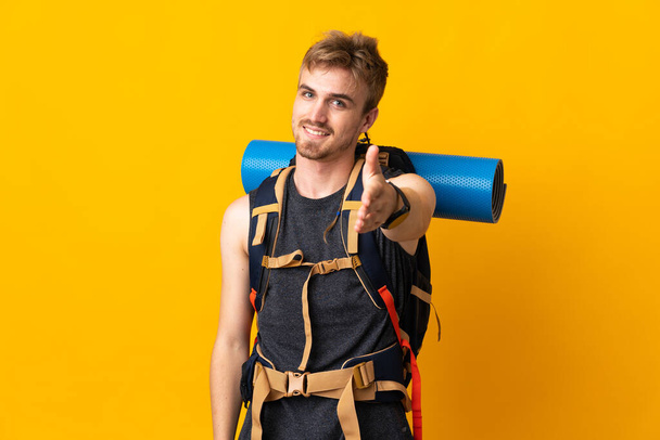 Jovem montanhista homem com uma grande mochila isolada no fundo amarelo apertando as mãos para fechar um bom negócio - Foto, Imagem