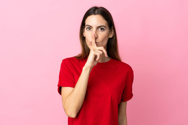 Young caucasian woman isolated on pink background showing a sign of silence gesture putting finger in mouth - Fotografie, Obrázek