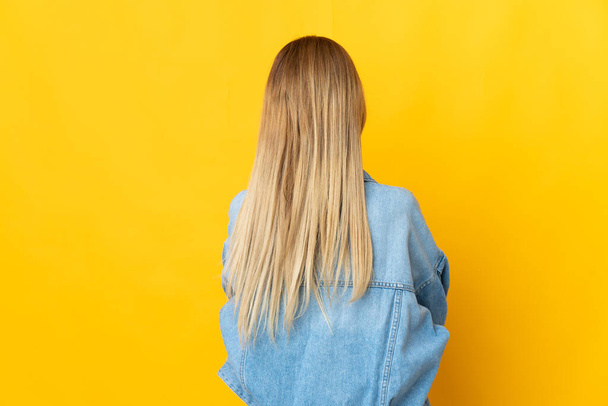 Jeune femme blonde isolée sur fond jaune en position arrière - Photo, image
