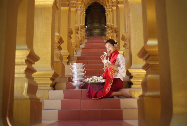 Myanmar kobiety trzymające kwiaty w świątyni. Południowo-wschodnia Azjatycka młoda dziewczyna z birmańską tradycyjną sukienką odwiedzająca buddyjską świątynię - Zdjęcie, obraz