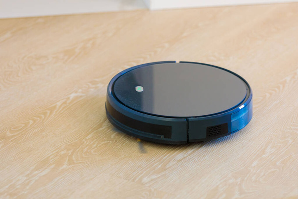 The circular robot vacuum cleaner collects debris from the living room floor. - Foto, Imagen