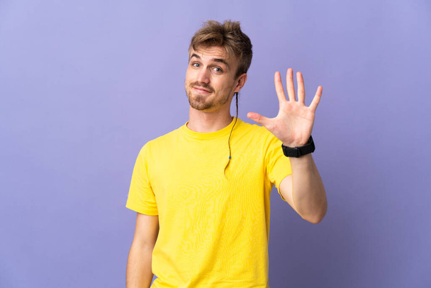 Jeune homme blond beau isolé sur fond violet comptant cinq avec les doigts - Photo, image