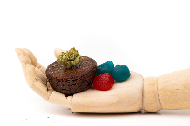 Mano de madera sosteniendo una pila de gomitas CBD y un brownie de olla con brote de mariguana - Foto, Imagen
