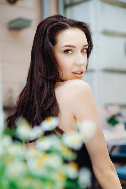 Attractive young woman glancing back over her shoulder. Pretty girl smiles outdoors. Blurred daisies in the foreground. Adorable brunette young woman. Vertical shot. - 写真・画像