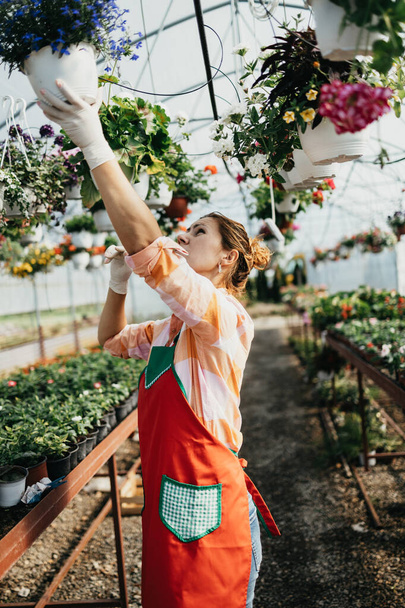 Happy and positive young adult woman working in greenhouse and enjoying in beautiful flowers. - Fotografie, Obrázek