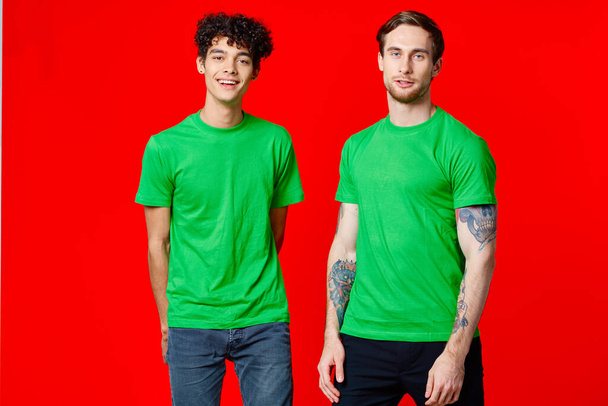 vreugdevolle vrienden in groene t-shirts staan naast rode achtergrond - Foto, afbeelding