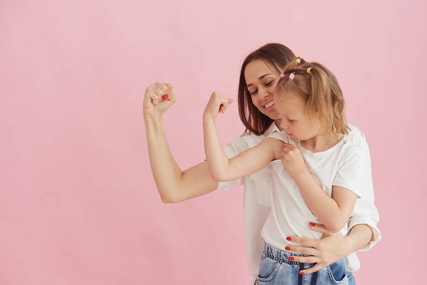 Familia divertida en el fondo de una pared de color rosa brillante. Madre y su hija pequeña divirtiéndose, mostrando que la fuerza de los músculos. Poder femenino, feminismo - Foto, imagen
