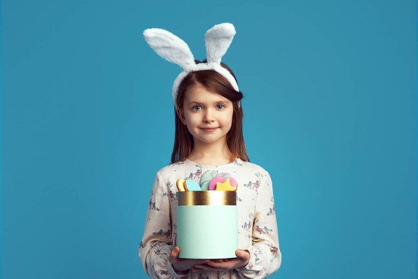 Dítě drží krabici se sušenkami, nosí králičí uši a roztomilé šaty - Fotografie, Obrázek